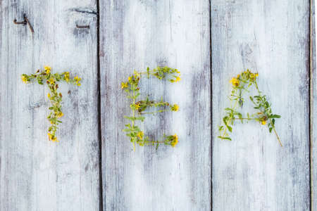 Word TEA is laid out from medicinal hypericum with yellow flowers on a wooden table. Healthy dried herbal drink. Top view.の写真素材
