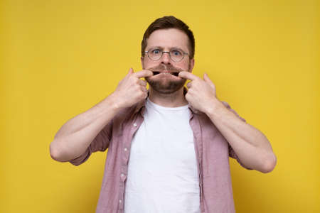 Whimsical man in glasses made a frightening grimace, he put fingers in mouth and, holding it open, looked into the camera.の写真素材