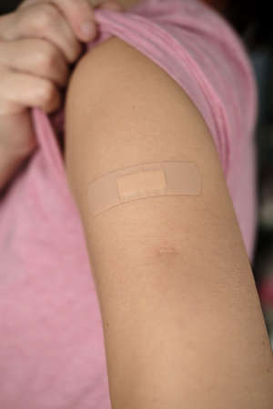 Hand after being vaccine . Woman lifts the sleeve of a t-shirt and shows her shoulder with a bandage after vaccination.の写真素材