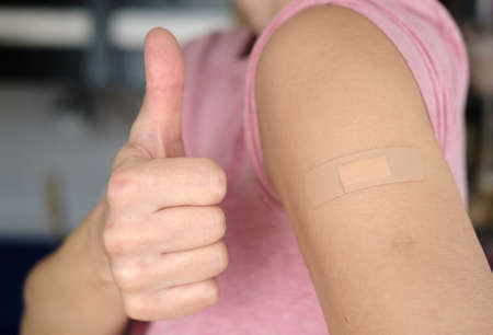 Close-up of a female shoulder with a bandage after a  vaccination and a gesture of approval, thumb up. Health concept.の写真素材