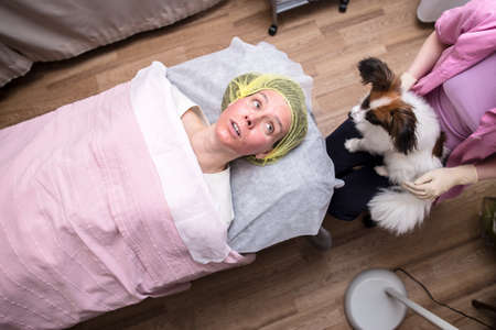 Woman with reddened skin at a beautician appointment does a rejuvenating procedure, chemical peeling and looks at a cute dog.の写真素材