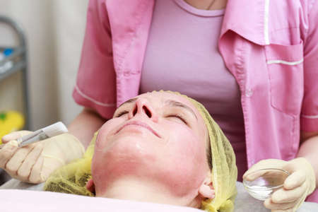 Professional beautician is going to apply a soothing mask with a brush to a patient reddened skin after a chemical peel.の写真素材