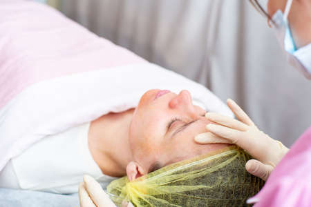 Beautician uses gloved hands to apply a chemical peeling solution to the patient face.の写真素材