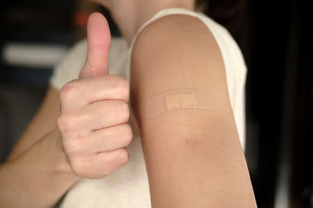 Close-up of a female shoulder with a bandage after a vaccination and a gesture of approval, thumb up. Health concept.の写真素材