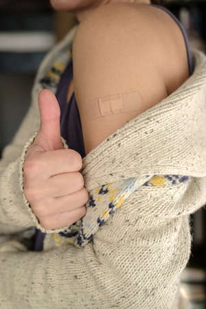 Woman showing shoulder with bandage after vaccination, making a gesture of approval, thumb up. Health concept. Close-up.の写真素材