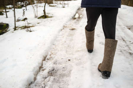 Men feet in warm felt boots walk along a snow-covered village road.