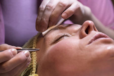Makeup artist plucking eyebrows with tweezers of a woman after a cosmetic procedure.の写真素材