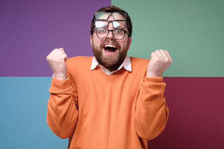 Strange man put on three pairs of glasses, he is pleasantly surprised, rejoices, laughs and makes a victory gesture with hands.の写真素材