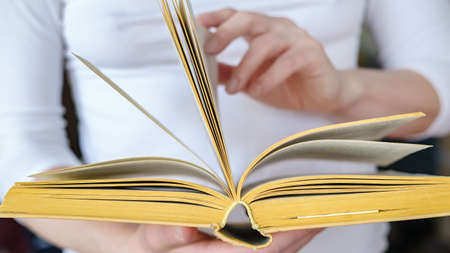 Open thick, old book of yellow in female hands, on a blurred background.の写真素材