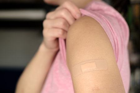 Hand after being vaccine . Woman lifts the sleeve of a t-shirt and shows her shoulder with a bandage after vaccination.の写真素材
