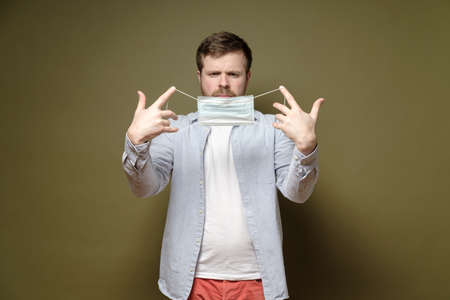Man with a serious look about to put on a medical mask to protect against a dangerous virus. Health concept.の写真素材