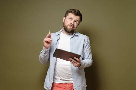 Handsome man with a tablet and a stylus pen is pondering an idea, he is thoughtful and unsure.Green background.の写真素材