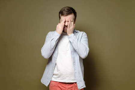 Man is depressed, he is unhappy and sobs, wiping the tears from his eyes with hands. Psychological health concept.の写真素材