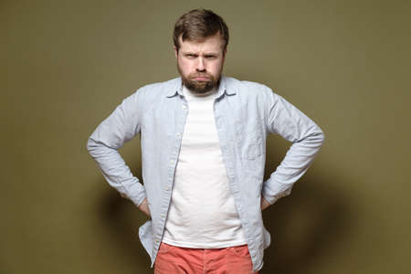 Caucasian bearded man frowned, he is dissatisfied with something and looks angrily with his hands on hips. Green background.の写真素材