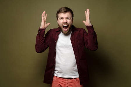 Caucasian bearded man is annoyed, he shouts furiously and makes a gesture with his hands. Green background.の写真素材