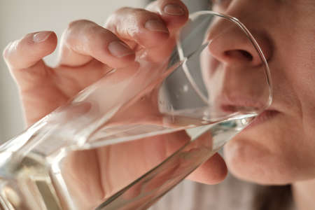 Close-up face of a woman drinking fresh, clear water from a glass. Health concept.の写真素材