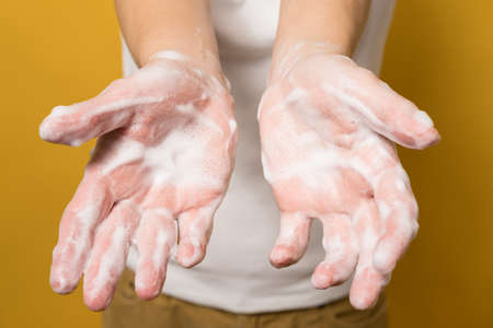Woman shows her hands in soapy suds, on a yellow background. Concept for an effective way to prevent the spread of infections. Close-up.の写真素材