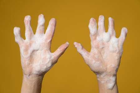 Hands covered with soapy foam. Isolated, on a yellow background. Concept for an effective way to...