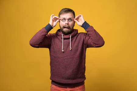 Funny Caucasian bearded man put on a toy rim of glasses without lenses and made a bizarre grimace. Yellow background.の写真素材