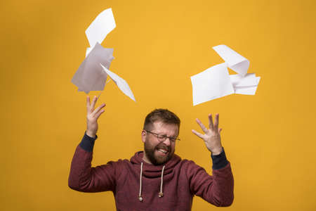 Man is stressed, he throwing a stack of white paper up, squeezes eyes shut and clenching her teeth. Bad working day. Copy space.の写真素材
