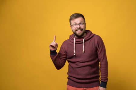 Benevolent, smiling man points finger up, he has an idea and he is glad about it. Copy space. Yellow background.の写真素材