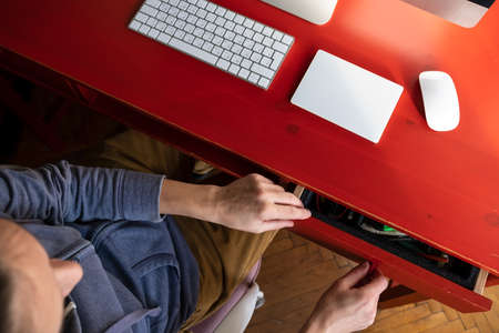 Woman opens a desktop drawer and wants to take something from there, on which there is a keyboard, touchpad and a computer.の写真素材