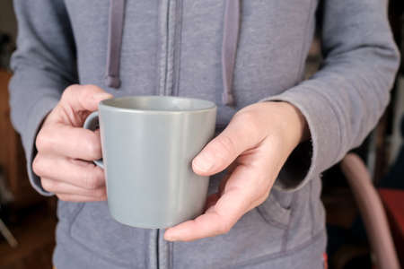 Female hands hold a mug of hot drink in the early morning in the apartment.の写真素材