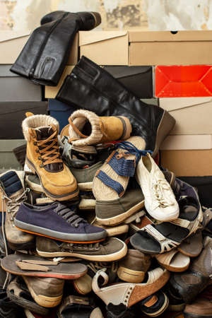 Heap of old, assorted shoes on stacked shoeboxes. Isolated, on the background of an old tattered wall.の写真素材