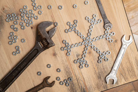 Snowflake made of metal nuts and wrenches on a wooden table. Winter symbol. New Year and Christmas holiday wait concept. Top view.の写真素材