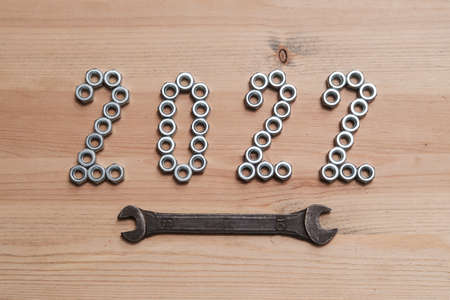 New Year 2022 Numbers are lined with metal nuts on a wooden table and emphasized with a wrench. Top view.の写真素材