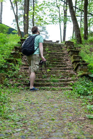 Tourist with a camera in his hands and a city backpack stands in front of the ancient stone steps and enjoys beautiful views.の写真素材