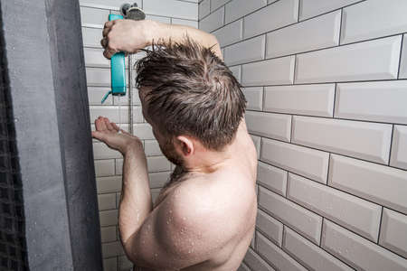 Caucasian man pours shampoo into his palm, stands in the shower, under a stream of water. Hygiene concept.の写真素材