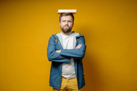 Pensive, funny male student put a book on his head as if it were a graduate hat and dreams of...