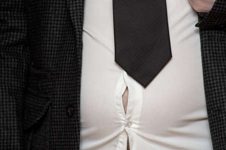 Male excess belly fat will soon rip his shirt. Overweight man. Concept of proper nutrition and a healthy lifestyle.の写真素材