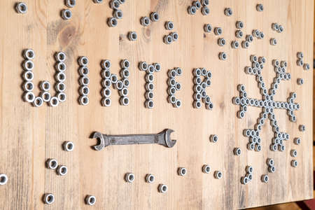 Word winter and a snowflake are lined with metal nuts on a wooden table, next to a wrench. New Year and Christmas holiday wait concept.の写真素材