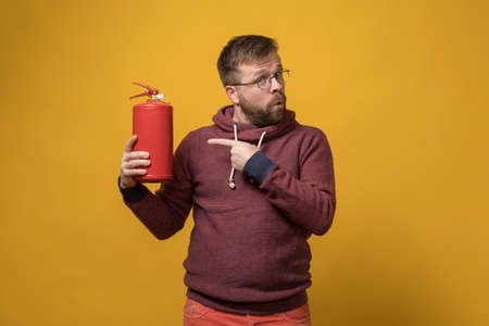 Man in glasses holds a fire extinguisher in hand and points very persistently at it with index finger.の写真素材