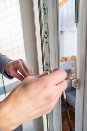 Woman hand with a screwdriver adjusts the metal fittings on a white PVC window. Close-up.の写真素材