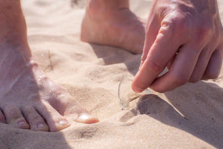 Barefoot man was walking along the beach and found a shard of broken glass from a bottle lying dangerously in the sand.の写真素材