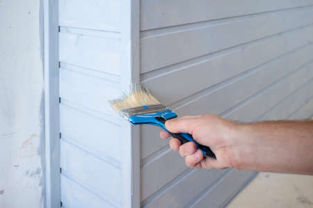 Hand paints with a brush a wooden wall in gray. Home renovation.の写真素材