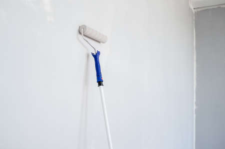 Roller on a wooden stick in gray paint is used to repaint the wall. Home renovation.の写真素材