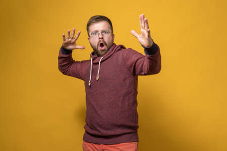 Shocked man makes an indignant hand gesture and swears at someone. Yellow background.の写真素材