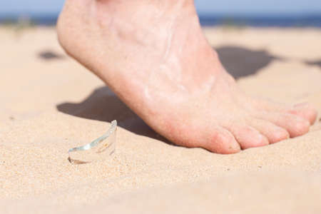 Leg walks on the beach and runs the risk of injury, stepping on a shard of broken glass of a bottle, which is lying on the sandy seashore.の写真素材