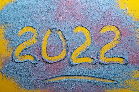 New year 2022 is written on a multicolored, bright powder on a yellow background. Top view.の写真素材
