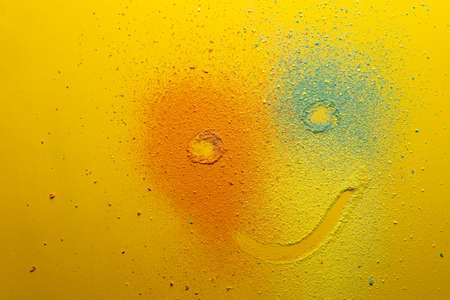 Cute emoticon that looks like a clown is drawn on a multicolored powder, on a bright background. Holiday concept. Copy space.の写真素材