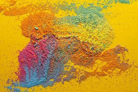 Mixture of multicolored powder is scattered randomly on a yellow background. Copy space. Abstract texture. Top view.の写真素材