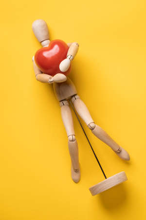 Small wooden figurine gently hugs a red tomato in the form of a heart, a symbol of love, lying on a yellow background. Top view.の写真素材