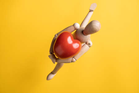 Wooden figurine runs, hugging a large red tomato in the form of a heart, a symbol of love. Yellow background. Romantic message.の写真素材