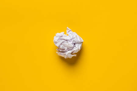 Crumpled sheet of white paper on a yellow background. Copy space. Top view.