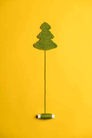 Knitted Christmas tree - a symbol of the New Year, with an unwound spool of thread like a trunk, on a yellow background. Copy space.の写真素材