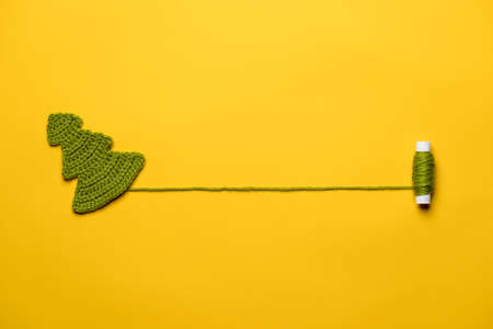 Knitted Christmas tree - a symbol of the New Year, with a spool of thread, with a place for text, on a yellow background. Copy space.の写真素材